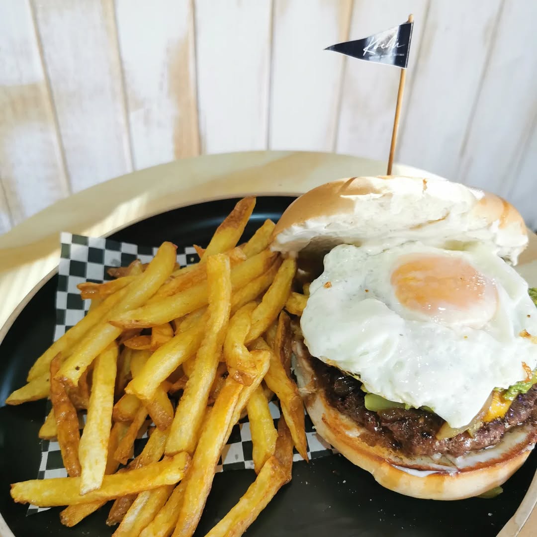 Hamburguesa armada con huevo frito e ingredientes a elección, acompañada de papas fritas, servida en Kochü, restaurante en Vichuquén con vista al Lago